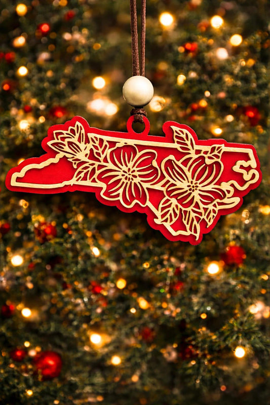Red North Carolina state ornament with laser-cut dogwood flower overlay, hanging on a Christmas tree