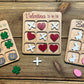 Set of three holiday-themed wooden tic-tac-toe boards displayed on a rustic wood surface. Designs include Valentine’s Day with hearts and X’s, St. Patrick’s Day with shamrocks and pots of gold, and Easter with bunnies and eggs. Perfect for holiday gifts, party favors, and stocking stuffers.