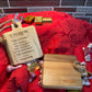 Rustic mini cutting board set displayed on a red fabric backdrop, featuring an engraved blessing and a plain wooden board, surrounded by chocolates.