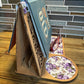Handcrafted wooden book stand with a laser-cut design, holding a sample book featuring a purple floral pattern on the base and glasses resting on the side.