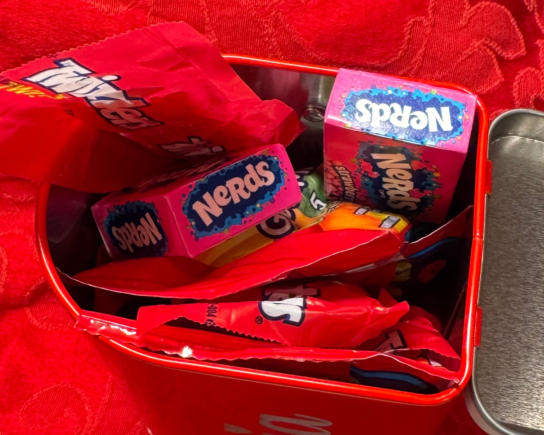 A close-up of a red mini tin mailbox personalized with the assorted non-chocolates inside the mailbox highlighting the mailbox as a customizable Valentine’s Day gift.