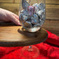Close-up of a wooden wine glass holder in use, securely holding a stemmed glass filled with chocolates, with the engraving 'Enjoy' visible.