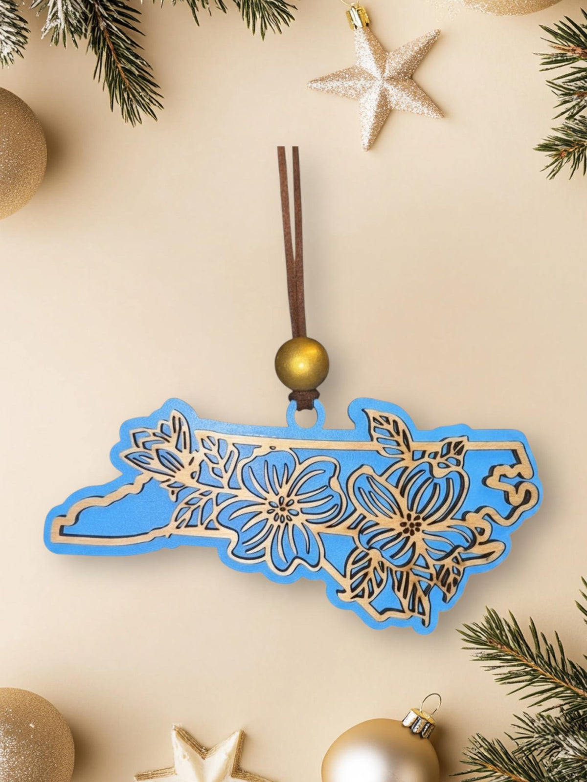 Sky Blue North Carolina dogwood ornament on a cream background with holiday decorations