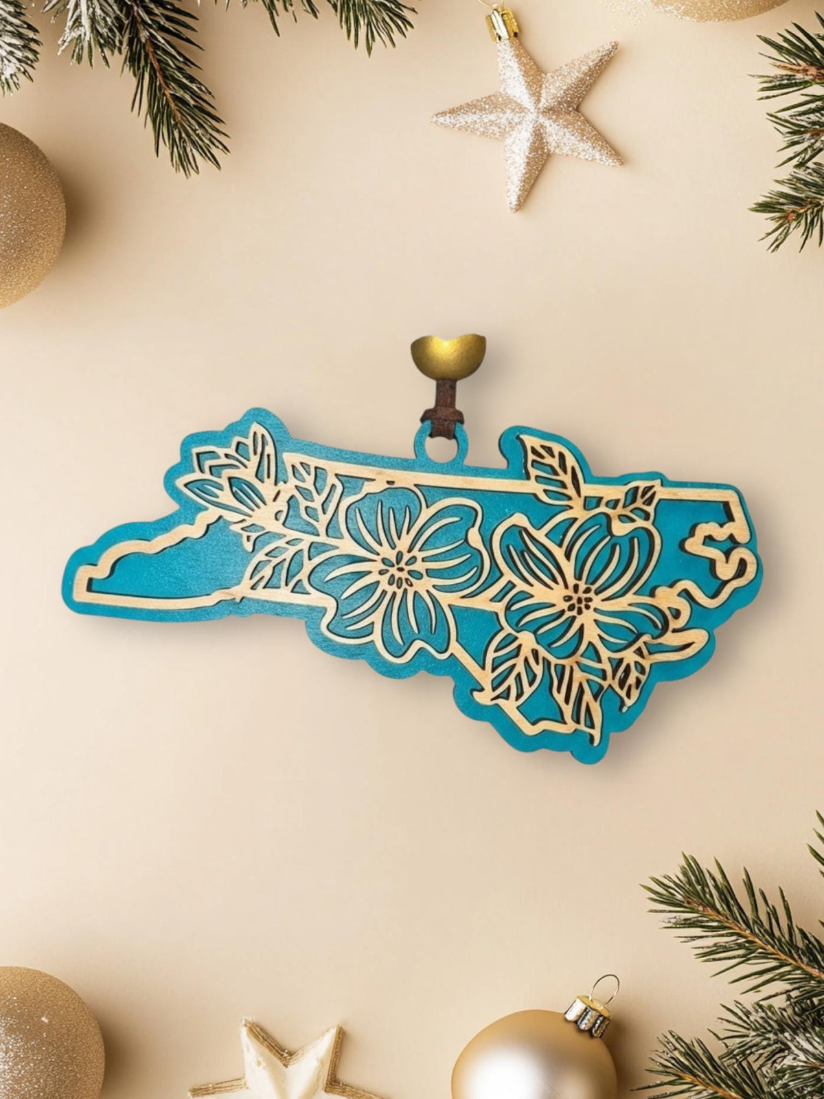 Teal North Carolina dogwood ornament on a cream background with holiday decorations