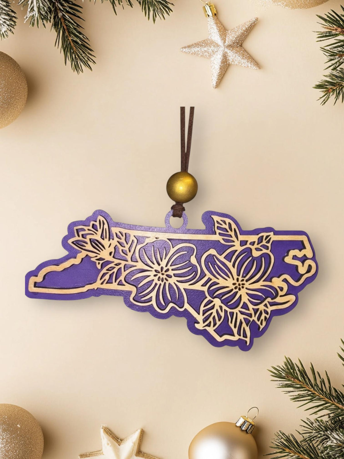 Purple North Carolina dogwood ornament on a cream background with holiday decorations