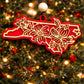Red North Carolina state ornament with laser-cut dogwood flower overlay, hanging on a Christmas tree
