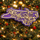 Purple North Carolina state ornament with laser-cut dogwood flower overlay, hanging on a Christmas tree