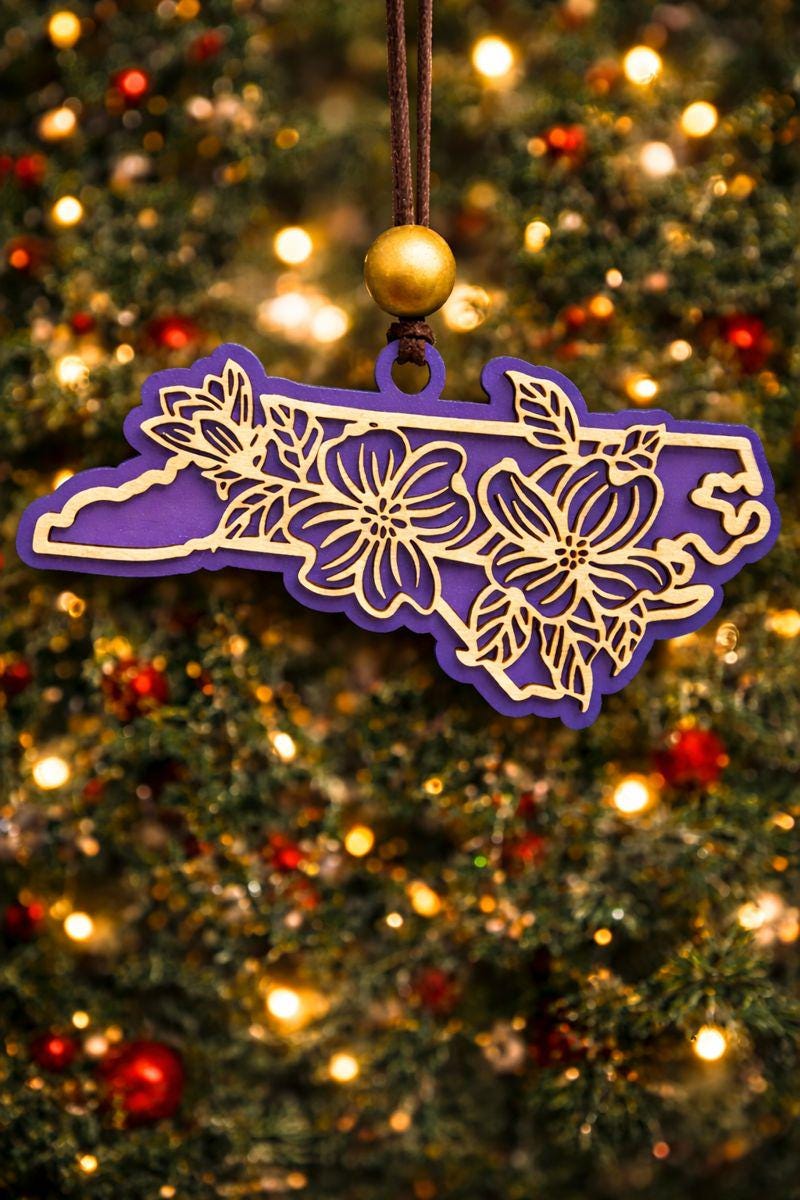 Purple North Carolina state ornament with laser-cut dogwood flower overlay, hanging on a Christmas tree