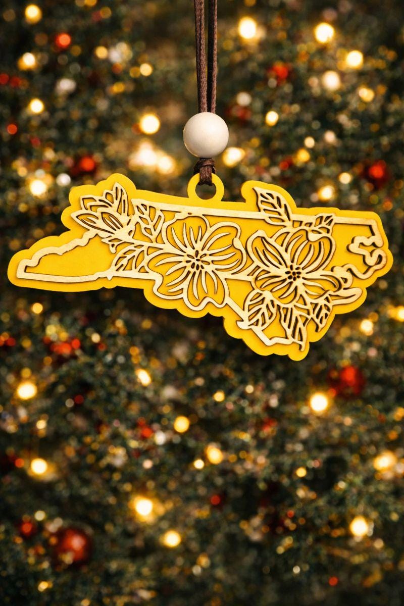 Yellow North Carolina state ornament with laser-cut dogwood flower overlay, hanging on a Christmas tree