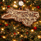 Walnut North Carolina state ornament with laser-cut dogwood flower overlay, hanging on a Christmas tree