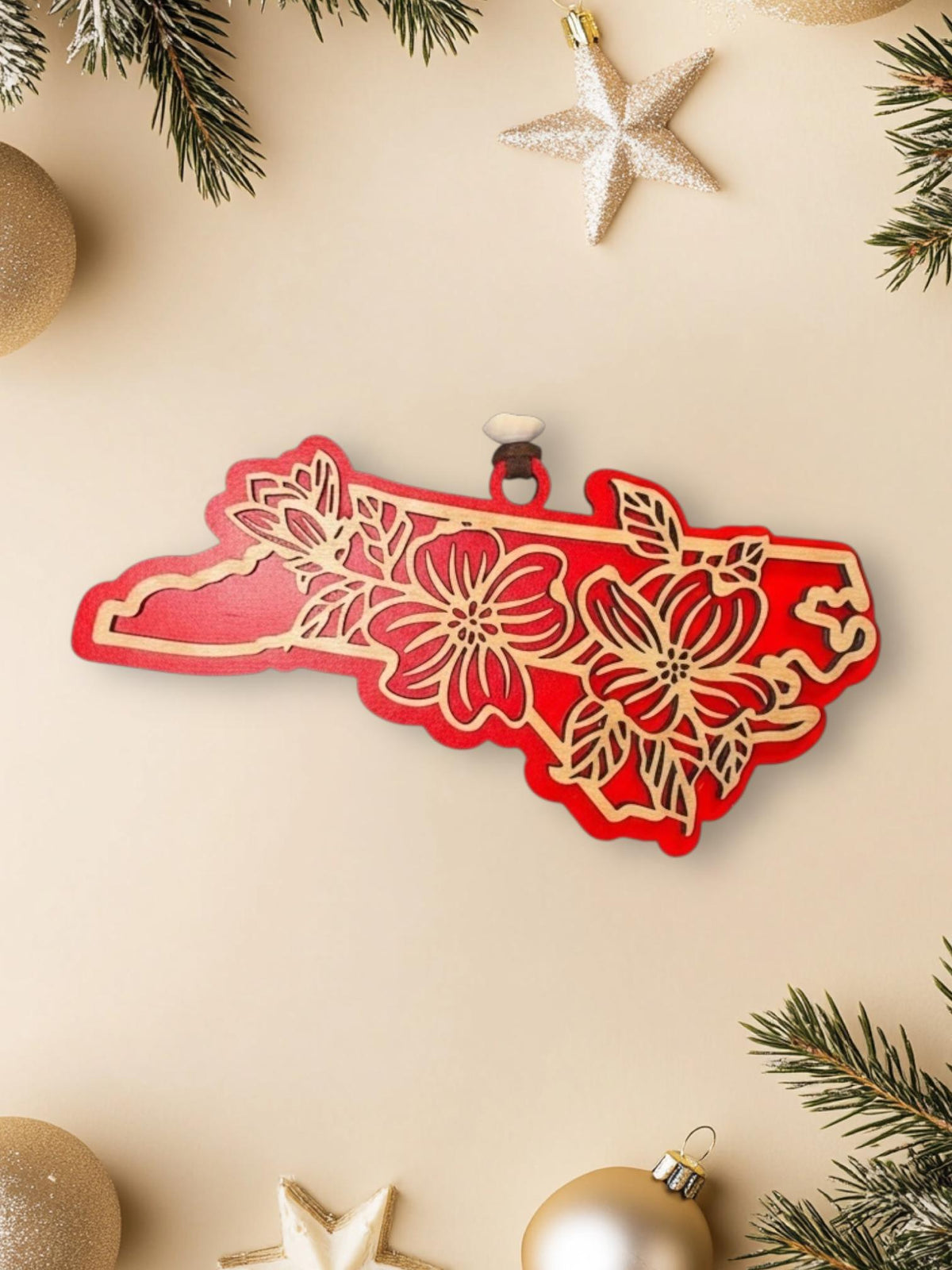 Red North Carolina dogwood ornament on a cream background with holiday decorations