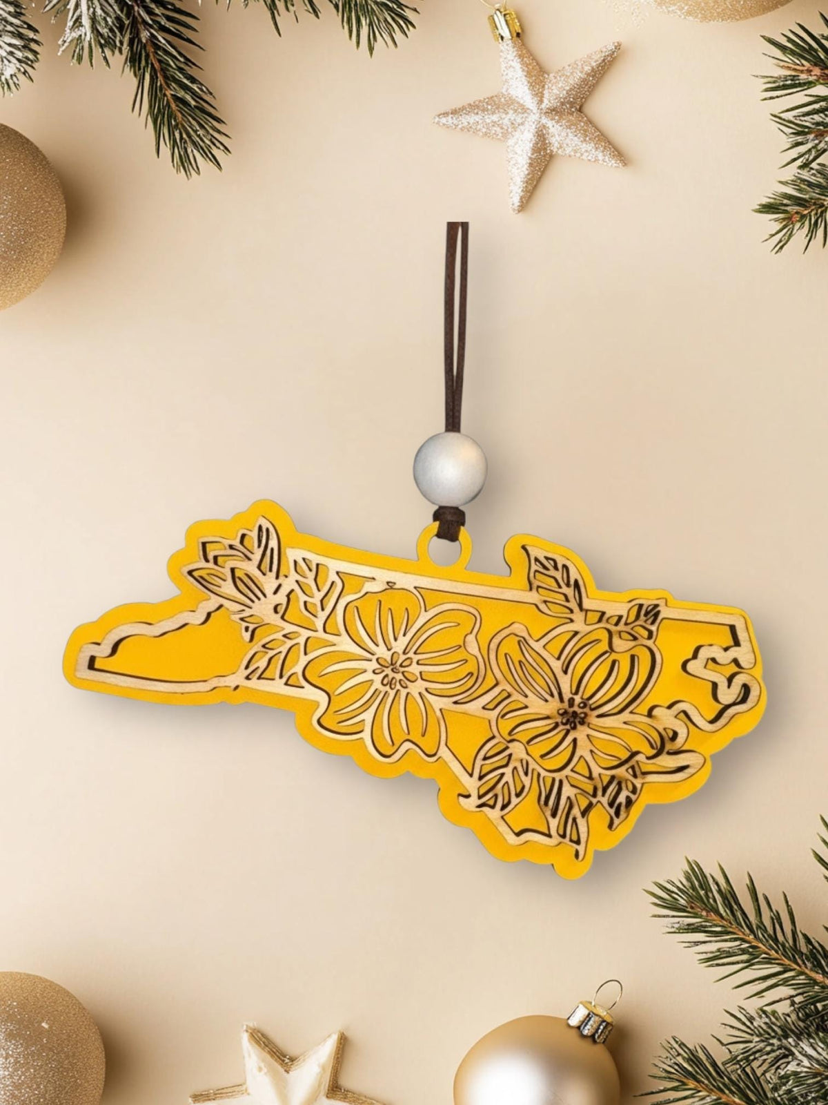 Yellow North Carolina dogwood ornament on a cream background with holiday decorations